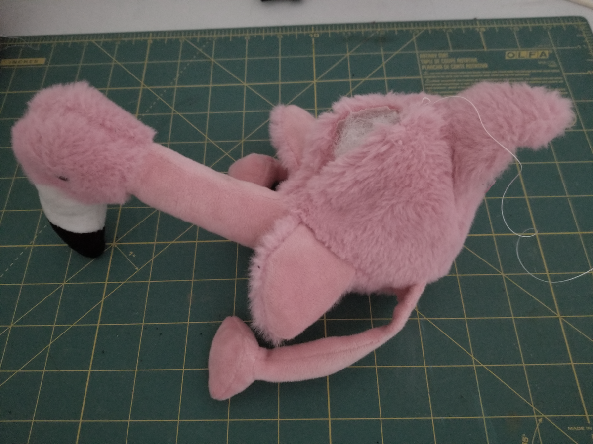 A flamingo stuffed toy is sitting on a cutting mat.